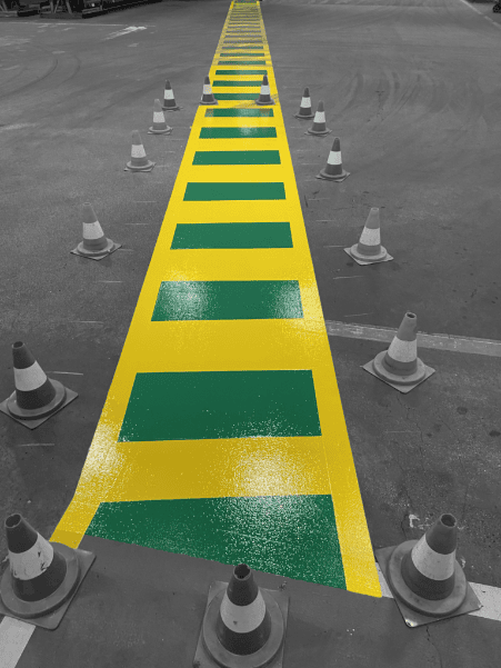 Ein Industrieboden mit einer markierten gelb-grünen Sicherheitszone, die von Verkehrskegeln abgegrenzt wird.