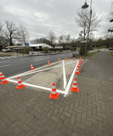 Ein neu angelegtes Sperrkreuz, abgesichert durch Leitkegel, inmitten einer friedlichen Ortschaft. Die Markierung sorgt für Struktur und Sicherheit im Straßenverkehr.