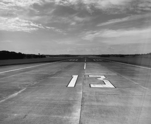 Ein Flugfeld welches eine große 13 inmitten hat, aufgebracht mittels einer Bodernmarkierung im Farbton RAL 9016 Verkehrsweiß.