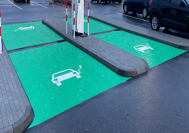 Bodenmarkierung im Außenbereich, die Elektroparkplätze kennzeichnet. Die Parkflächen sind vollständig in RAL 6024 Verkehrsgrün eingefärbt, mit einem Elektroauto-Piktogramm in RAL 9016 Verkehrsweiß, um eine klare und sichtbare Kennzeichnung für Elektrofahrzeuge zu gewährleisten
