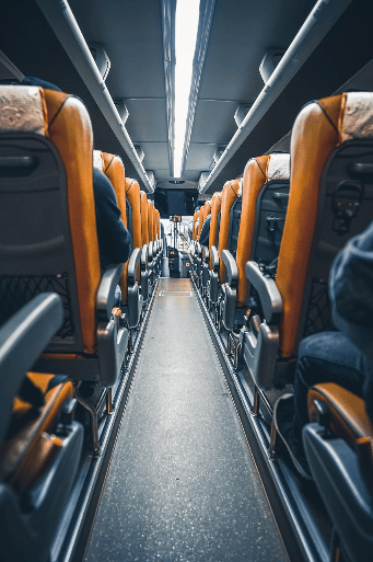 Innenansicht eines Reisebusses mit orangefarbenen Sitzen auf beiden Seiten und einem sichtbaren Gang in der Mitte.