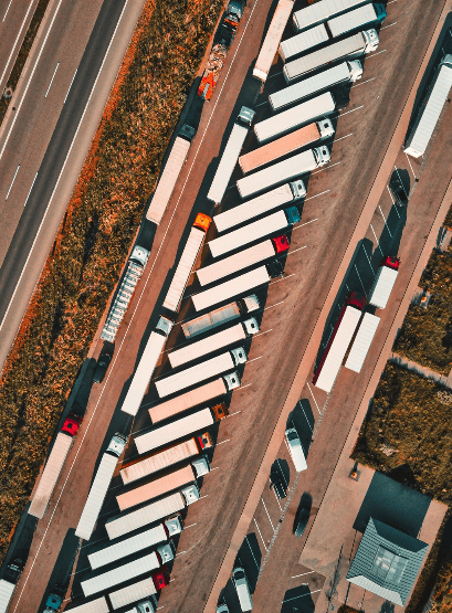 Luftaufnahme von LKW Parkplätzen, die geordnet genutzt werden, mit klaren Bodenmarkierungen und fließendem Straßenverkehr.